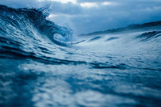 Ocean wave curling against cloudy sky