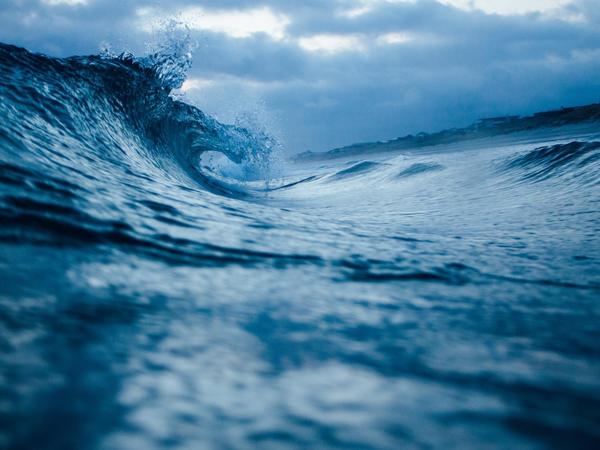 An ocean wave curling against a cloudy sky